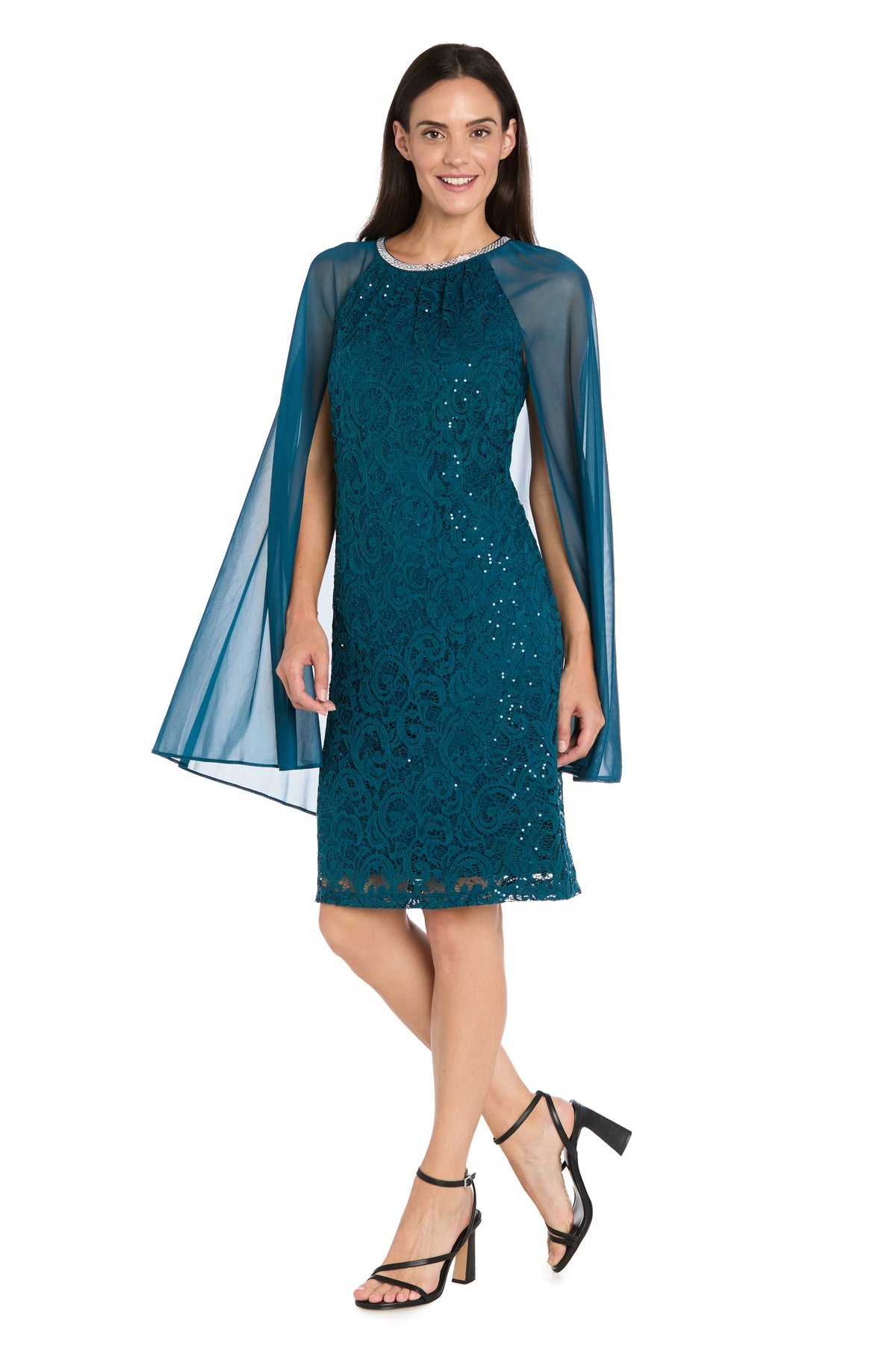 Woman wearing the R&M Richards 3864 Knee-Length Cape Party Dress in teal with sequin lace and sheer cape sleeves, paired with black heeled sandals, standing against a white background.